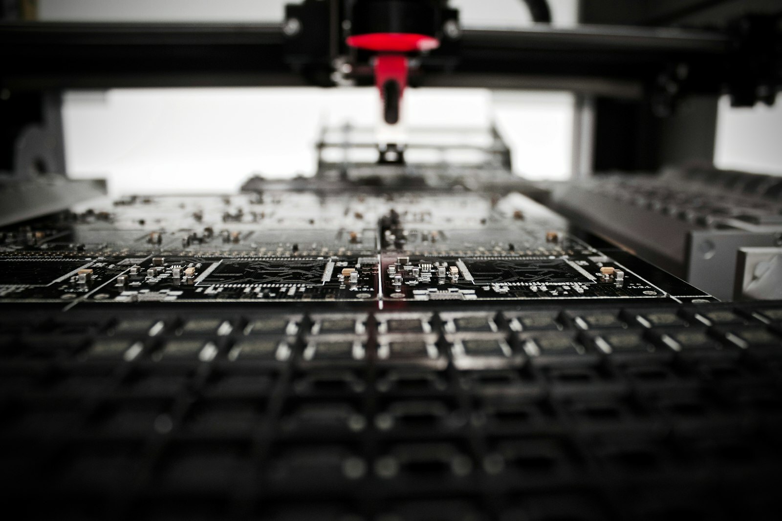 A robotic arm with a red nozzle above a black circuit board